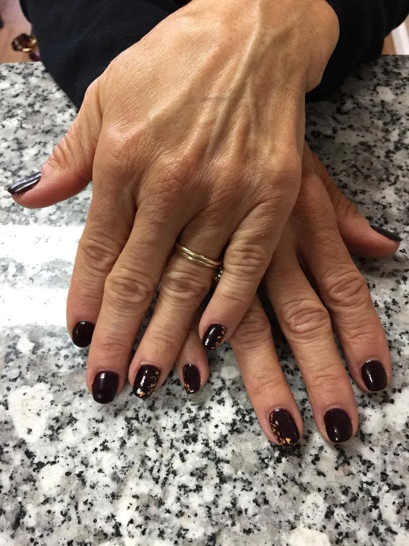 Short nails in dark plum gel, four of them flecked with gold foil