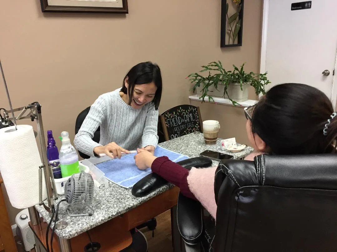 A nail technician filing a client’s nails at her table